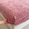 A close-up of a pink jacquard weave fitted sheet bedding with a floral pattern being touched by a hand.