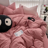 A pink duvet cover set with pillows and a black stuffed animal on a bed.