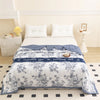 A white duvet cover with a blue floral pattern is displayed on a bed in a bright room.