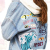 A denim jacket featuring embroidered cartoon pink iron-on patches on the sleeve and chest area.