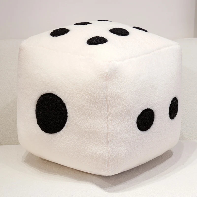 A white, cube-shaped plush toy resembling a die with black spots is displayed on a white surface.