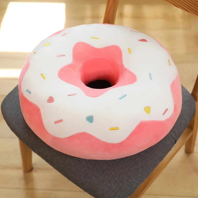 A pink and white plush pillow shaped like a frosted doughnut with colorful sprinkles.