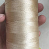 A hand holds a spool of beige high tenacity polyester sewing thread with a yellow plastic core.