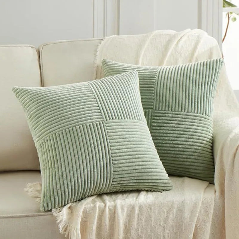 A close-up of a light sage green corduroy patchwork pillow cover resting on a white linen fabric.