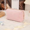 A pink textured cosmetic storage pouch with a gold zipper lies on a white rug.