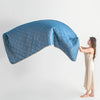 A light blue quilted cooling summer blanket is draped over a white surface, next to a person.