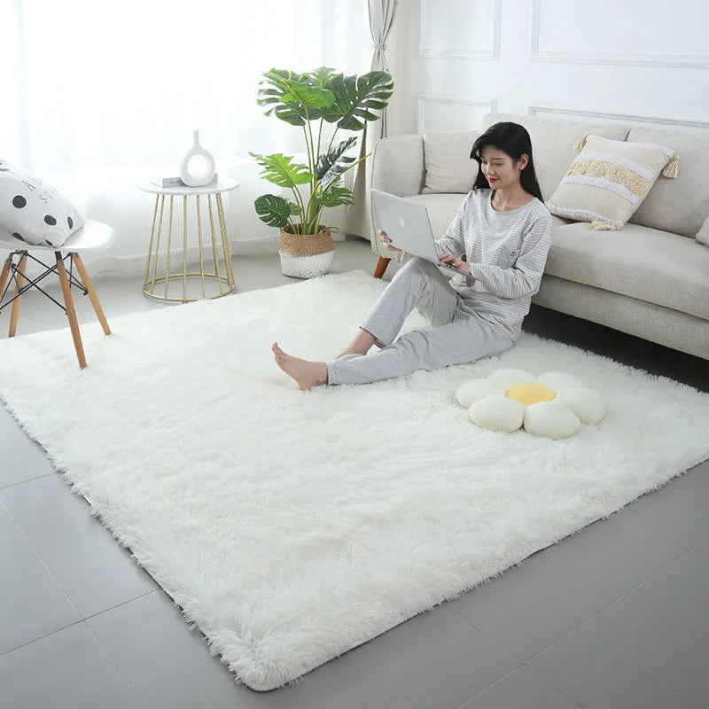 A woman relaxing on a white shag rug in a bright living room with a laptop and potted plant.