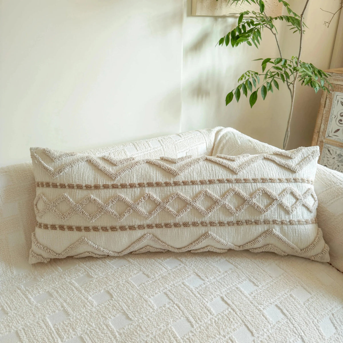 A cream knit pillow cover with geometric patterns and brown stripes resting on a light-colored sofa.