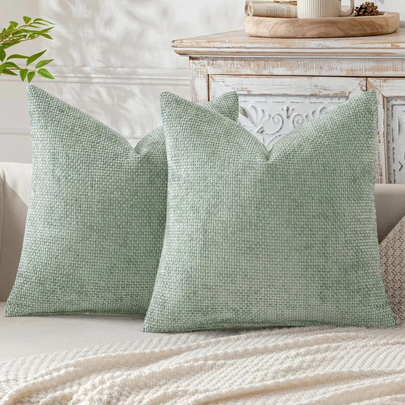 A pair of sage green chenille pillows with a minimalist design resting on a light-colored surface.