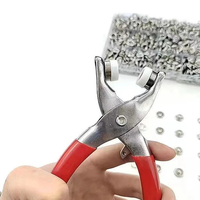 A hand holds a pair of silver pliers with red handles, next to a box of fasteners.