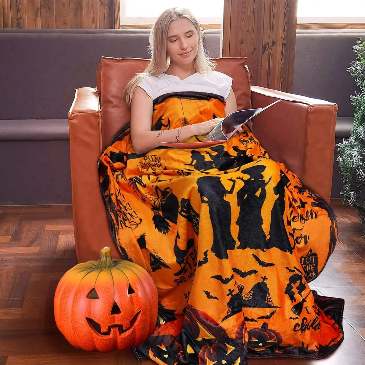 A woman sits in a brown leather armchair wearing an orange and black patterned flannel blanket.