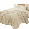 A beige large 6-layer cotton gauze blanket draped over a bed with white pillows.