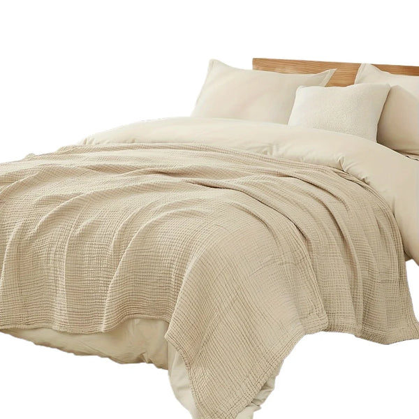 A beige large 6-layer cotton gauze blanket draped over a bed with white pillows.
