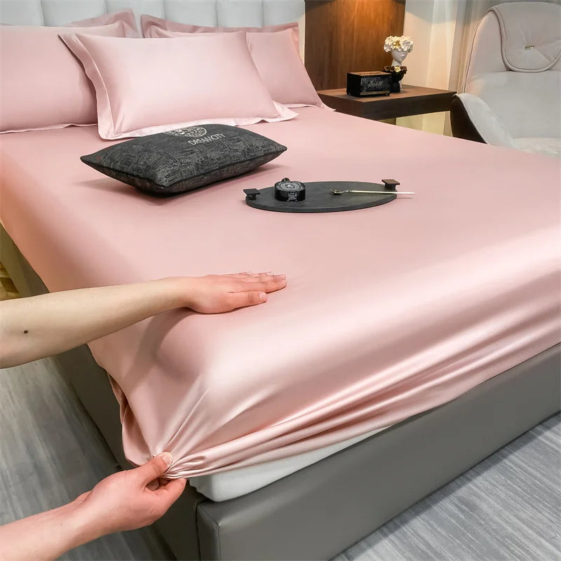 A pink fitted bed sheet is being adjusted on a bed, with pillows and a dark cushion visible.