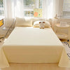 A light cream organic cotton bedding set featuring a flat sheet, pillows, and a small stuffed animal on a bed.