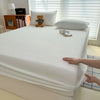A white fitted bed sheet cover is draped over a white mattress, with pillows and a teddy bear visible nearby.