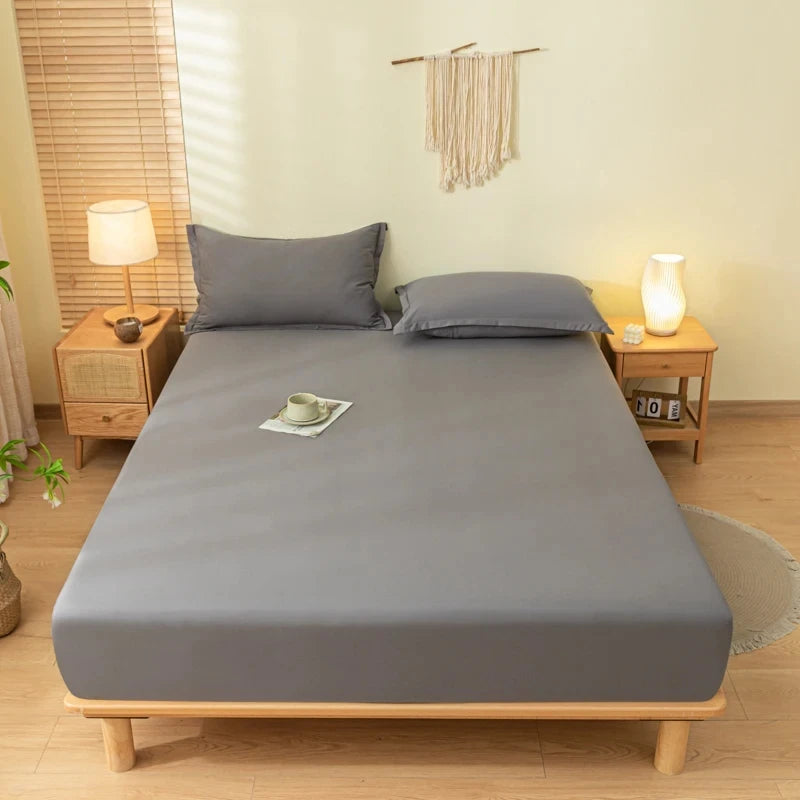 A gray fitted sheet set with pillowcases is displayed on a wooden bed frame in a bright bedroom setting.