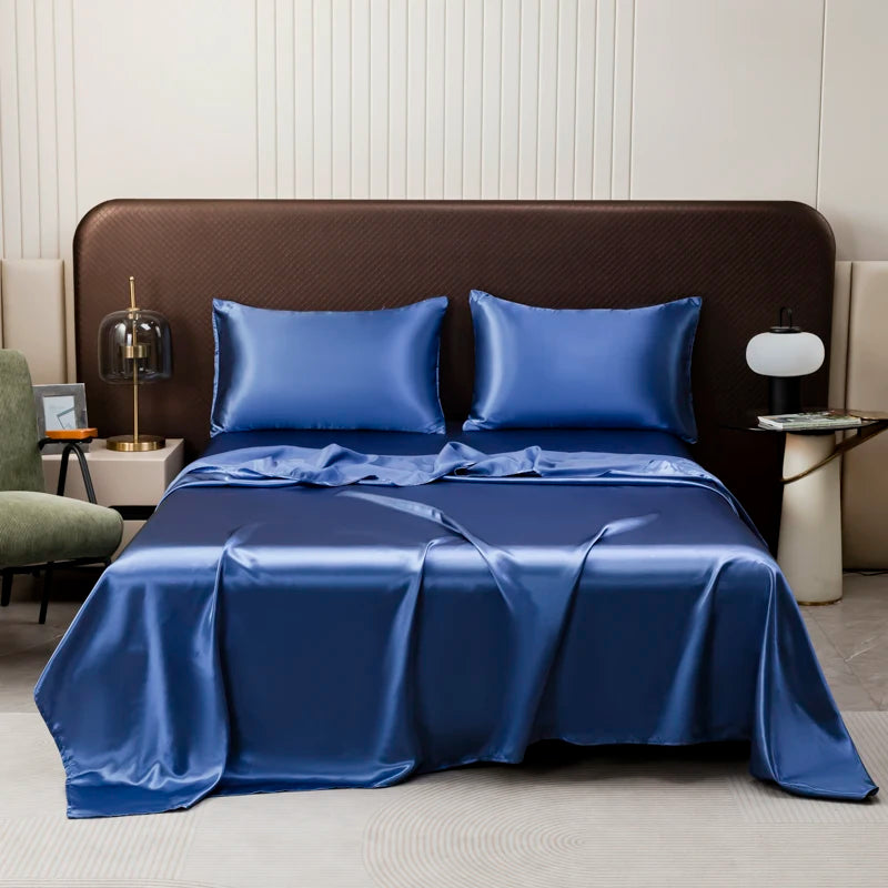 A luxurious royal blue satin flat bed sheet set is draped over a brown upholstered bed with white linens.