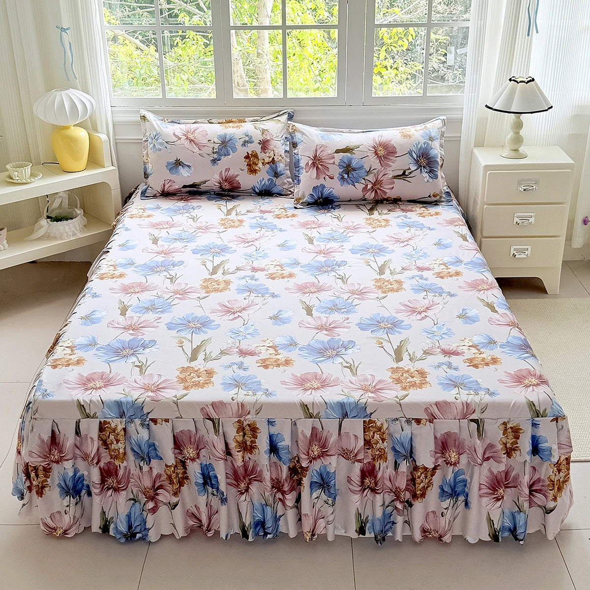 A bed featuring a white floral print skirt set with pink, blue, and rust colored flowers and matching pillows.