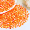 A pile of orange-red AB resin flatback rhinestones scattered on a white surface.