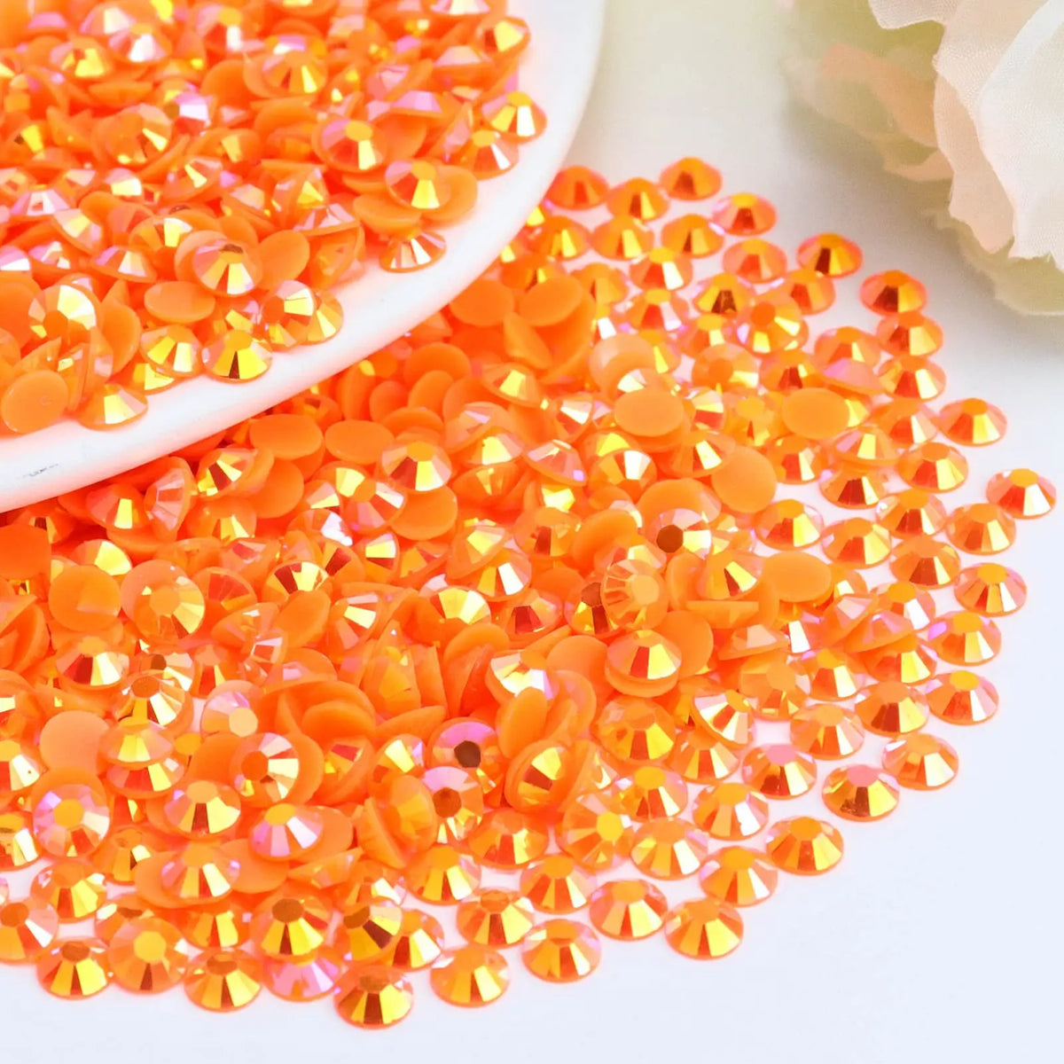 A pile of orange-red AB resin flatback rhinestones scattered on a white surface.
