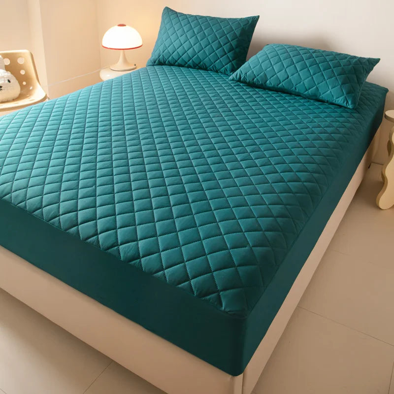 A teal quilted mattress protector is displayed on a bed, featuring diamond stitching and matching pillows.
