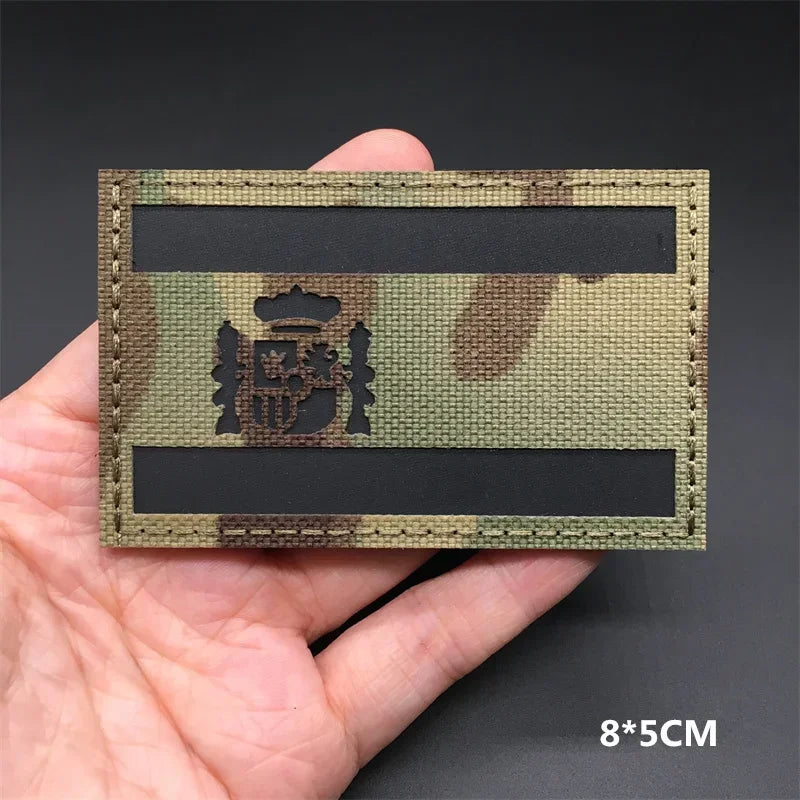 A rectangular tactical patch featuring a national flag design in camouflage colors on a dark background.