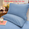 A light blue matte solid color pillowcase is displayed on a bed, next to a candle and flowers.