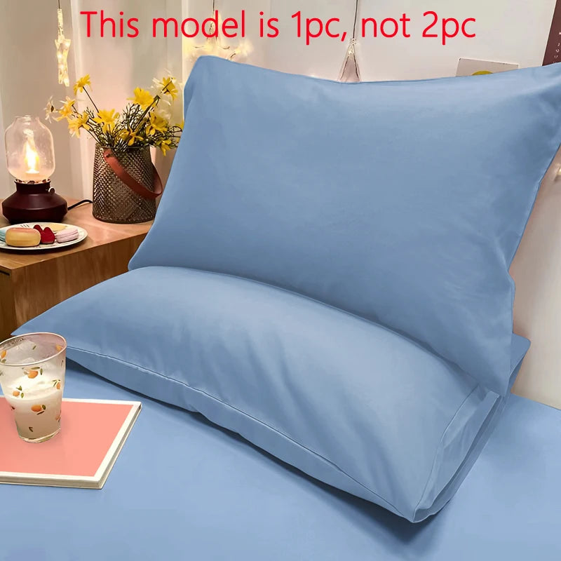 A light blue matte solid color pillowcase is displayed on a bed, next to a candle and flowers.