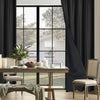 A set of floor-length black blackout curtains framing a bright window and dining area.