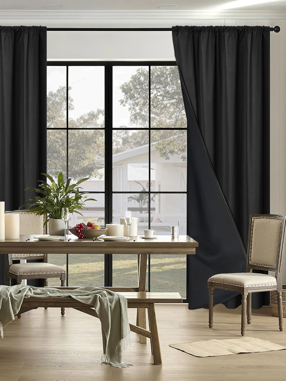 A set of floor-length black blackout curtains framing a bright window and dining area.