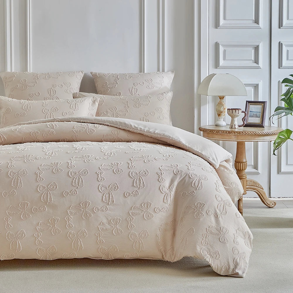 A beige luxury quilt duvet set with white embroidered details displayed on a bed against a white paneled wall.