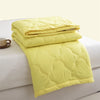 A stack of bright yellow quilted duvet covers or blankets on a white surface.