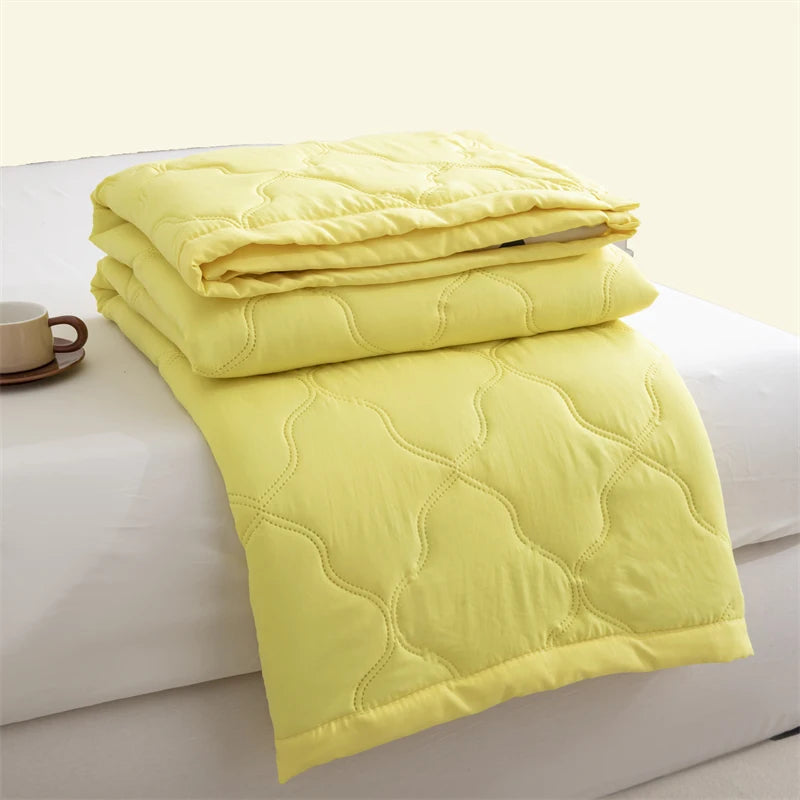 A stack of bright yellow quilted duvet covers or blankets on a white surface.