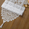 White retro lace table runner with delicate floral pattern and tassels on a wooden surface.