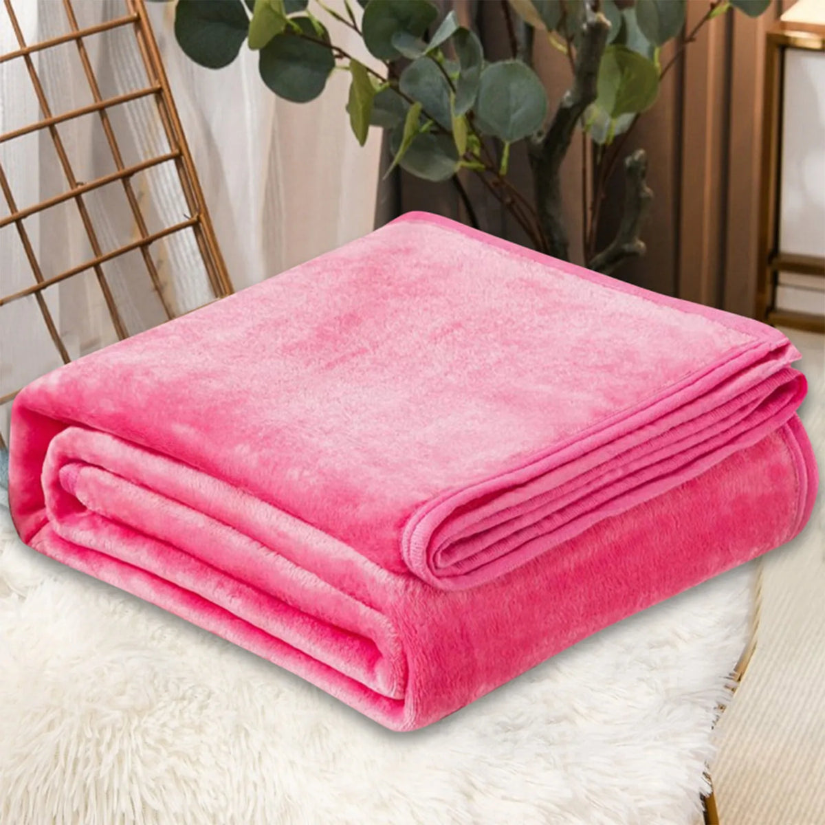 A bright pink coral fleece throw blanket folded neatly on a white fluffy surface.