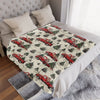 A red vintage truck Christmas throw blanket displayed on a bed with white pillows and gray bedding.