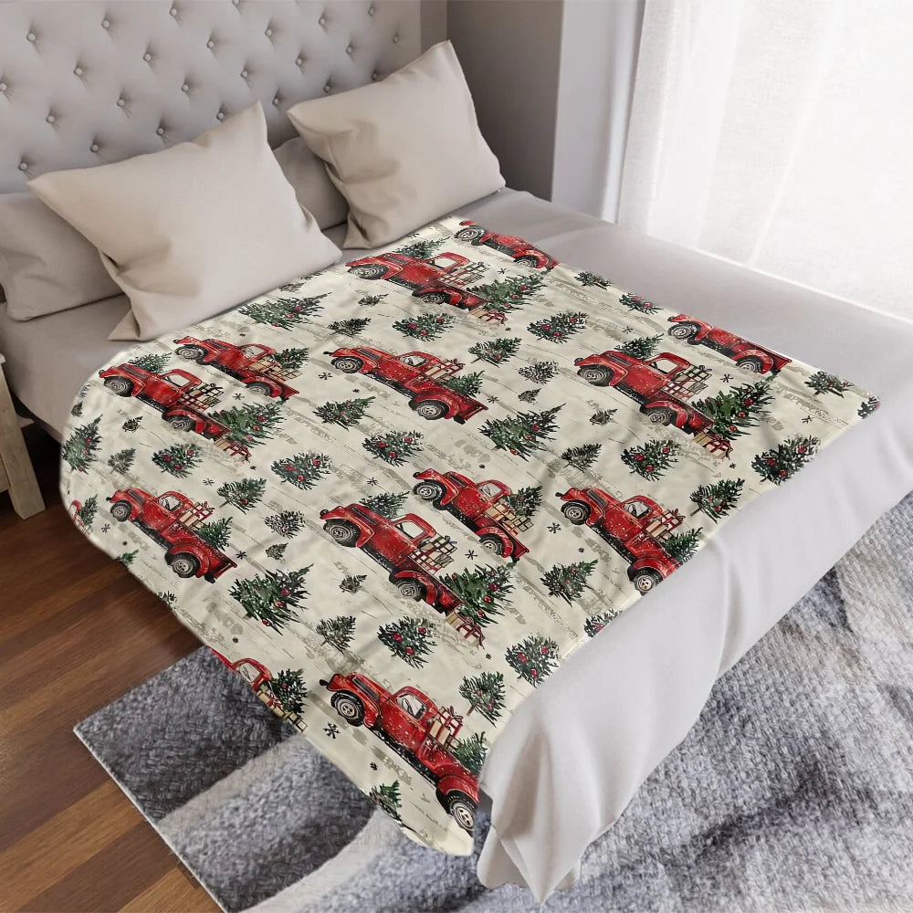 A red vintage truck Christmas throw blanket displayed on a bed with white pillows and gray bedding.
