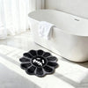 A black gothic sunflower absorbent non-slip bathroom mat placed on a white marble floor next to a white bathtub.