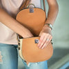 A person holds a tan leather bag with magnetic snap fasteners.