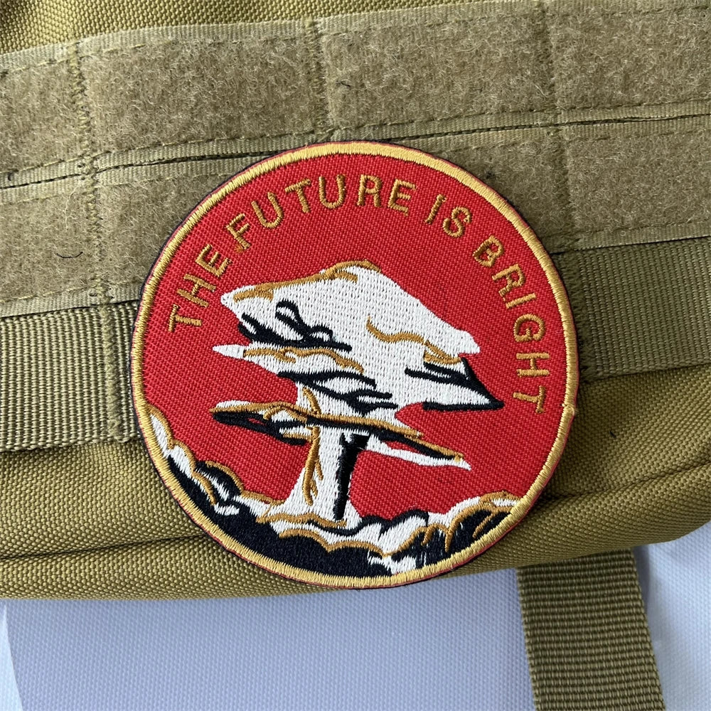 An embroidered patch with a white bird silhouette on a red background and the text THE FUTURE IS BRIGHT, attached to a khaki 