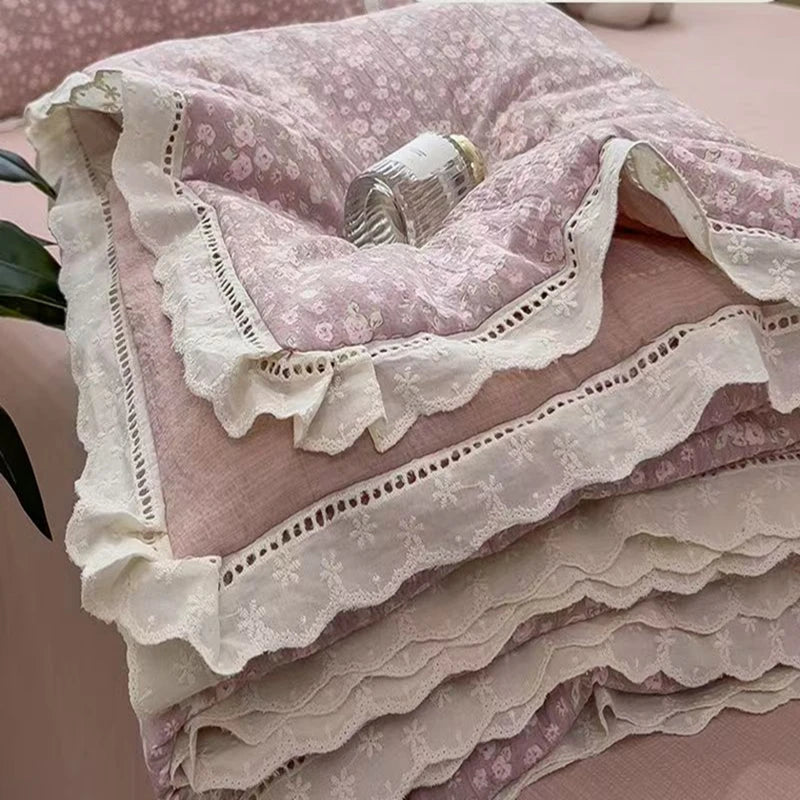 A stack of pink and white floral print quilt blankets with delicate lace trim.