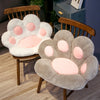 A plush bear paw cushion in gray and pink is displayed on a wooden chair.