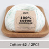 A ball of white organic cotton yarn labeled QJH 100% COTON ORANIQUE resting on a wooden board.