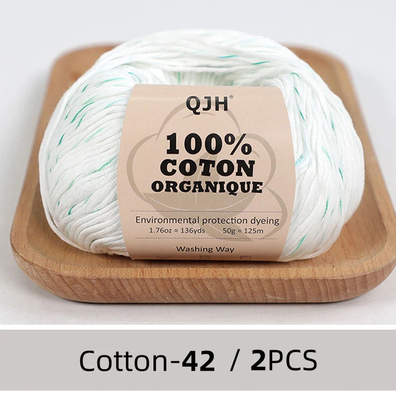 A ball of white organic cotton yarn labeled QJH 100% COTON ORANIQUE resting on a wooden board.