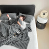 A woman is relaxing on a bed covered with a gray plush winter blanket and a black headboard.
