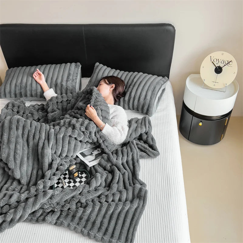 A woman is relaxing on a bed covered with a gray plush winter blanket and a black headboard.