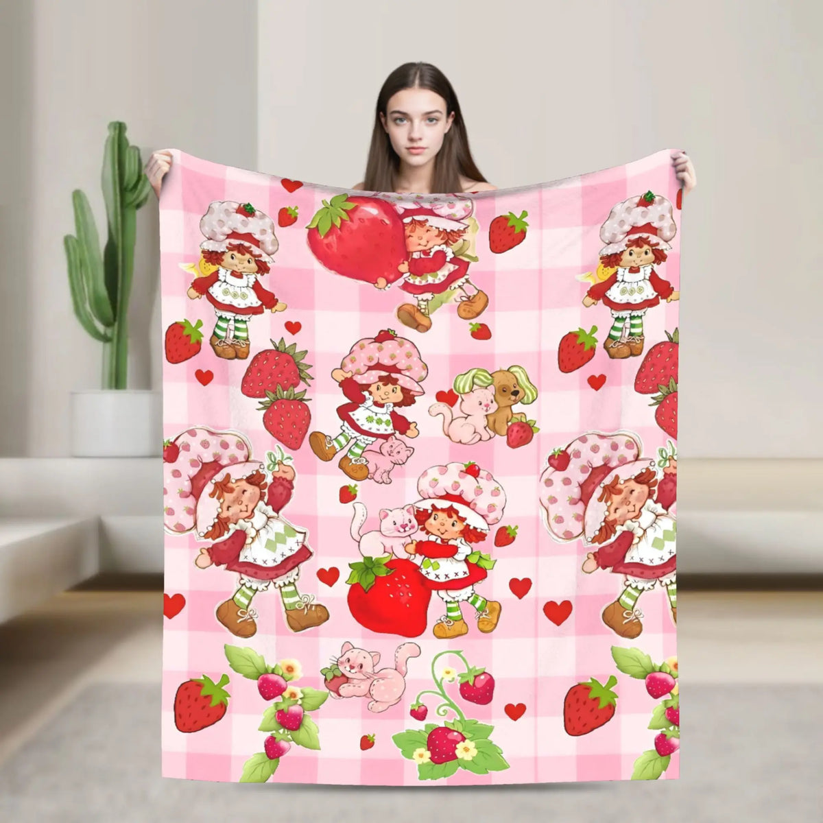 A pink plaid throw blanket featuring a pattern of strawberry shortcake characters and fruit.