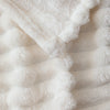 Close-up of a white and beige striped flannel throw blanket with fluffy texture.
