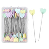 A clear plastic box containing numerous nickel-plated dressmaking pins with colorful heart-shaped heads.